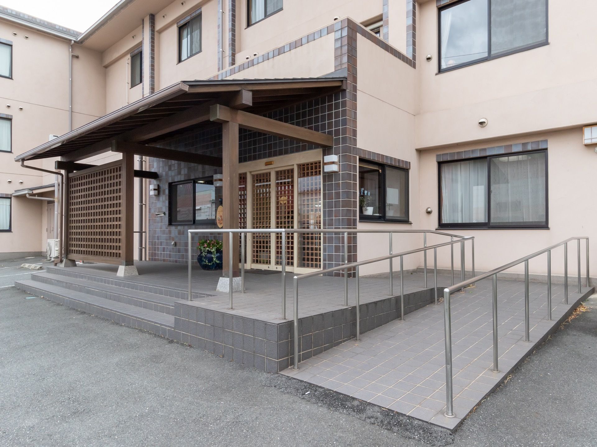エントランスのドア付近に格子を設置して、洋風な建物に和のテイストを加えている。安全対策として、階段とスロープの両方が設置してある。