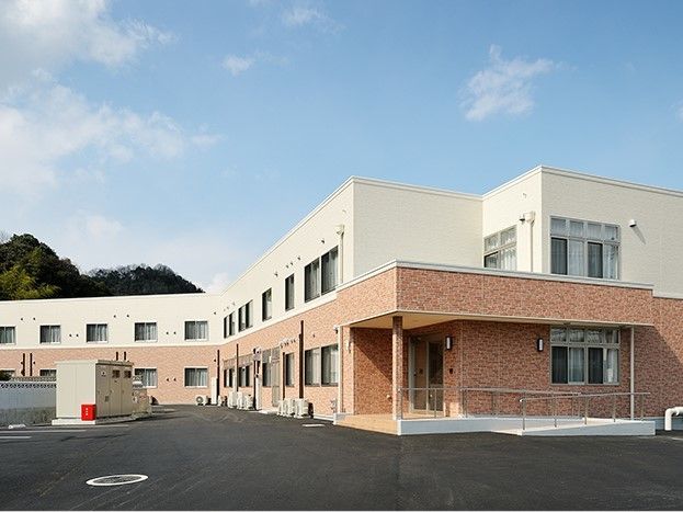 ブラウンとベージュの２階建ての建物は横に長く、大きい。周辺には緑も多くある。