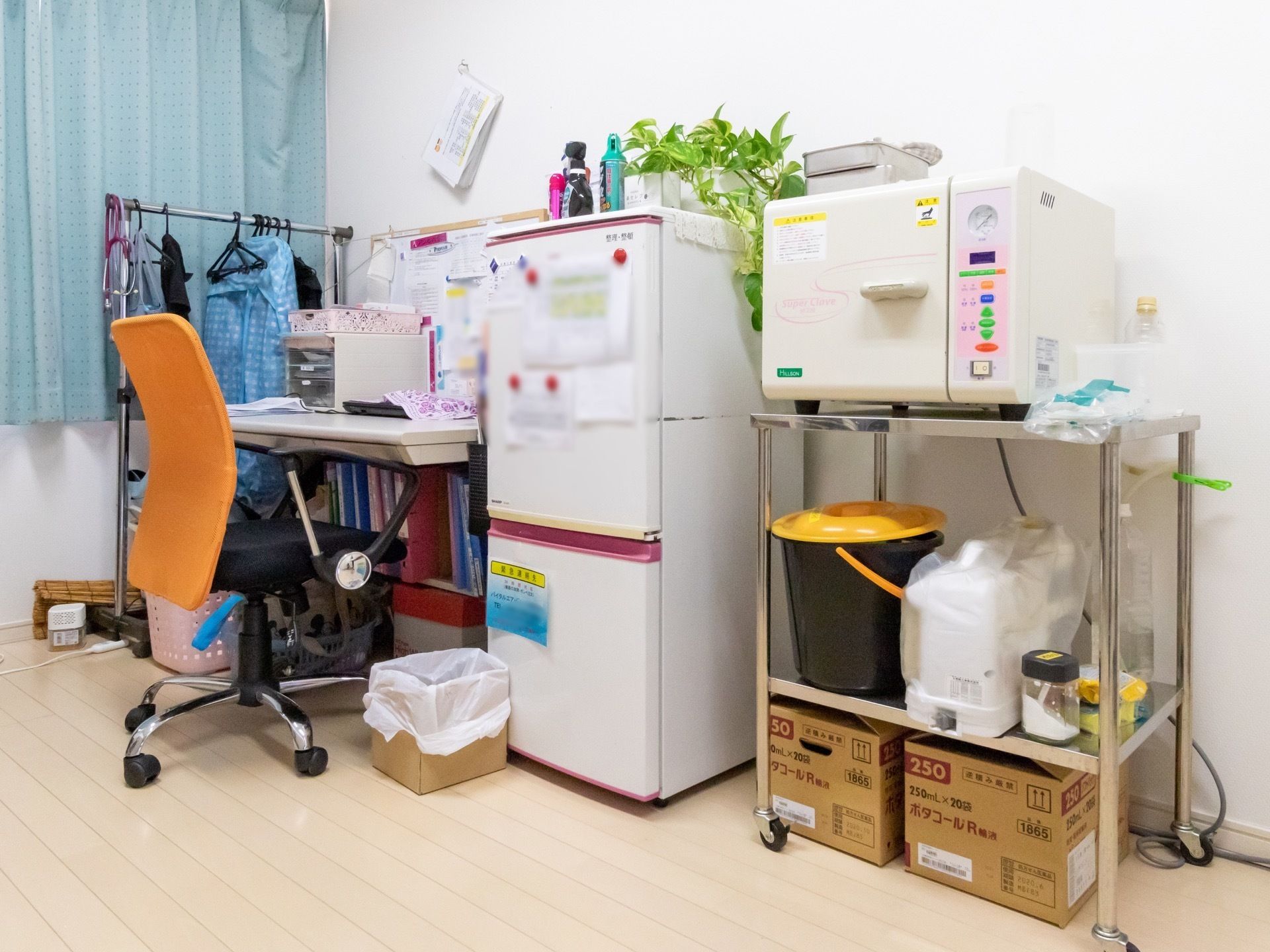 スタッフ用の作業机の周囲には、冷蔵庫やパイプハンガーが置かれている。冷蔵庫にはいくつかの文書が貼られている。