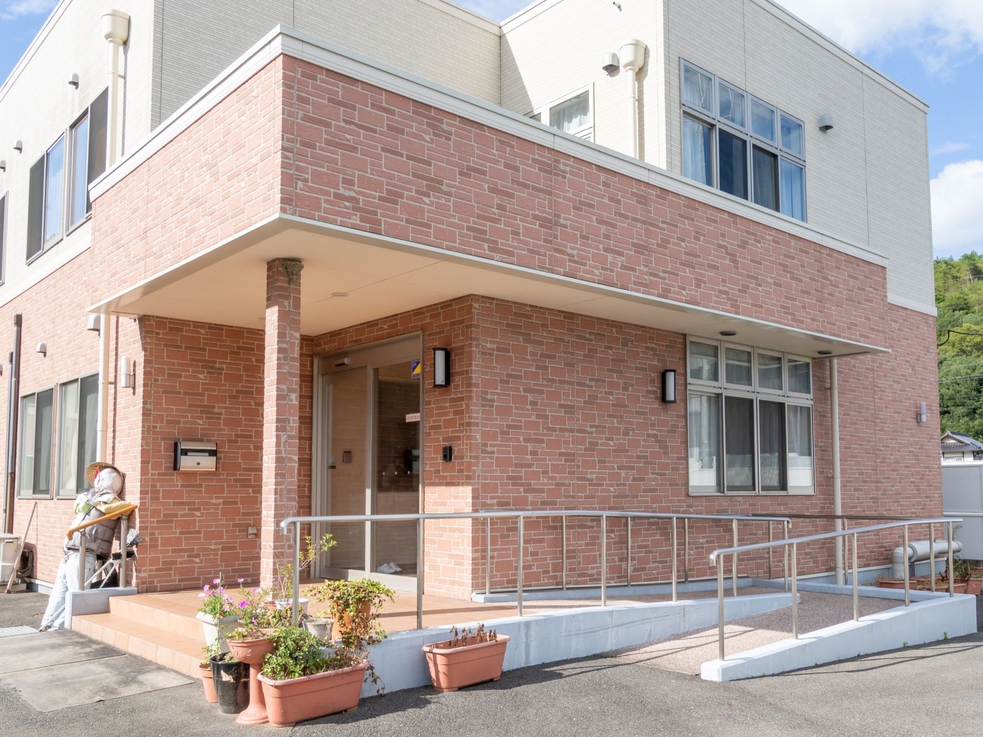 外部から施設内へのアプローチには、２段ほどの階段とスロープがある。スロープには手すりがある。