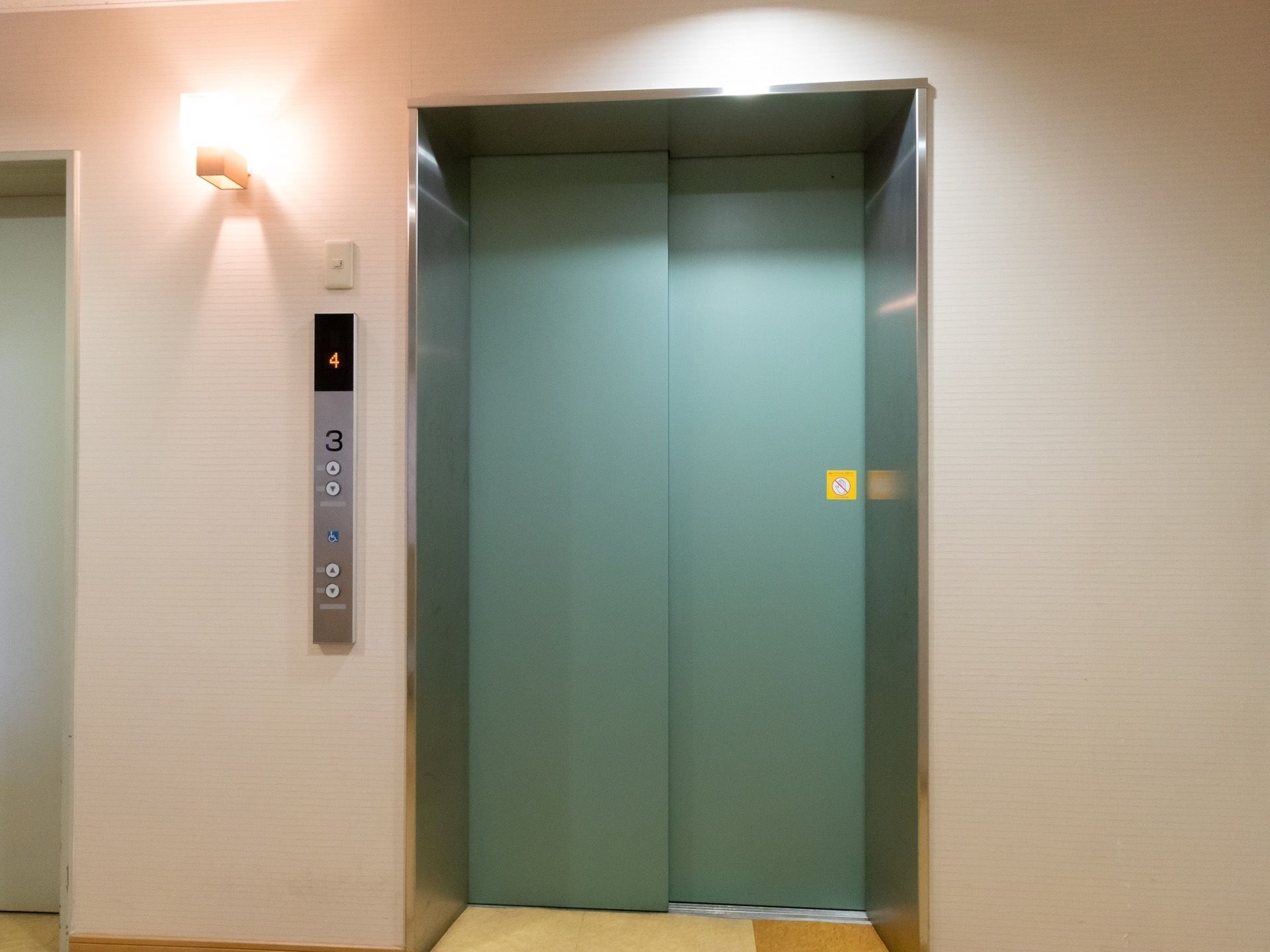 エレベーターの扉はグリーン系の色である。呼び出しボタンがあるプレートに、見やすいフォントで階数表示がされている。