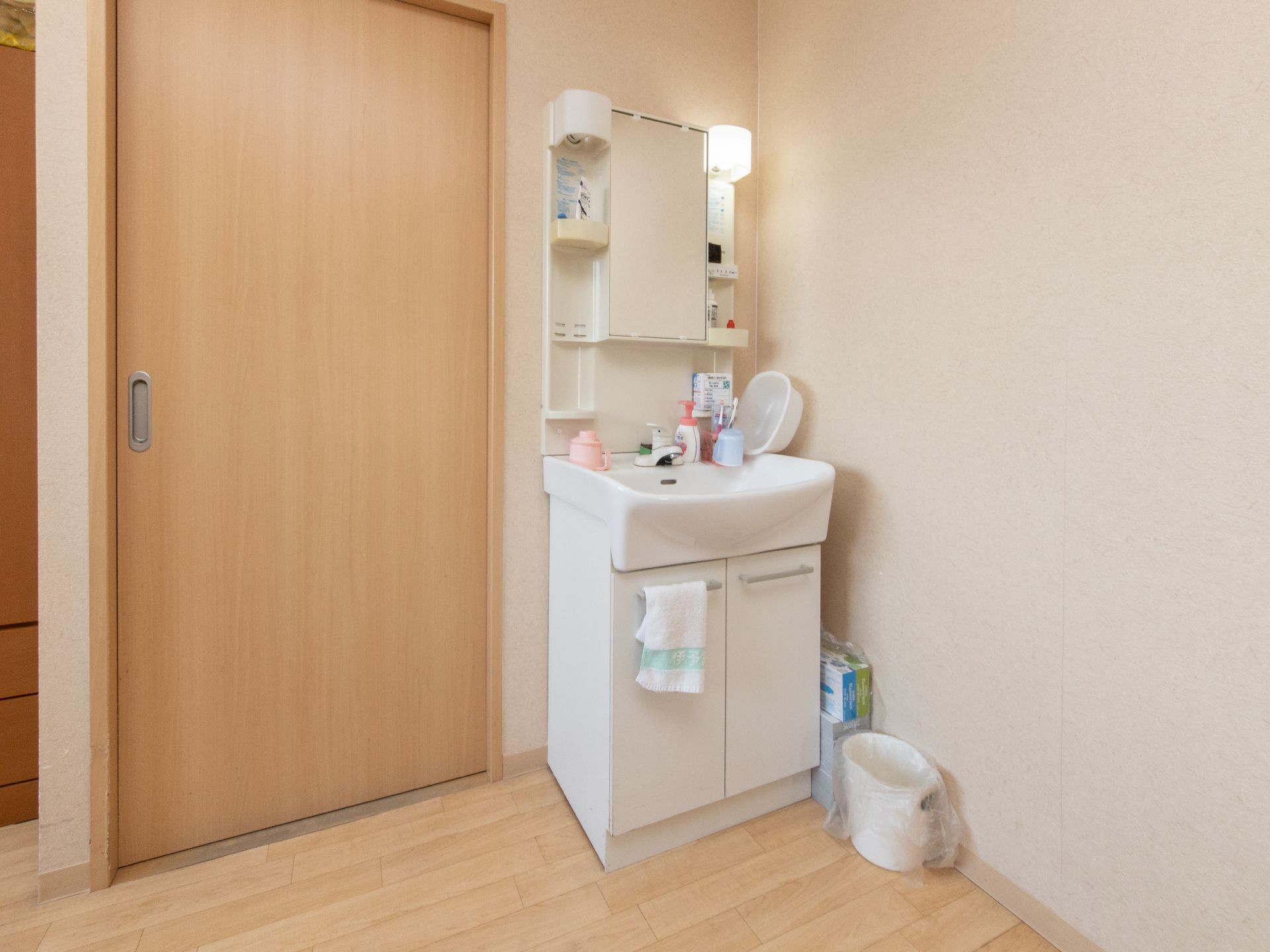 洗面台は白く清潔感がある。水栓はレバー式を採用しており、小物を置いておける棚があるので、使いやすく便利である。