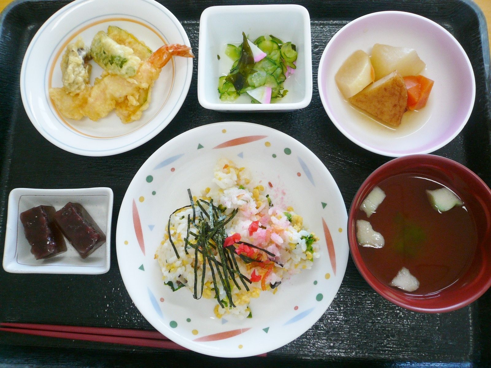 キュウリの酢の物や吸い物、天ぷら、ちらし寿司、羊羹のようなもの、煮物が並んでいる。