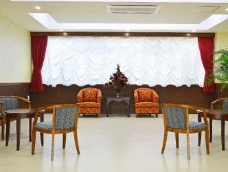 白とブラウンの部屋の奥にはレースと深紅のカーテンがかかっている。手前にはソファ、椅子とテーブルのセットが置かれている。