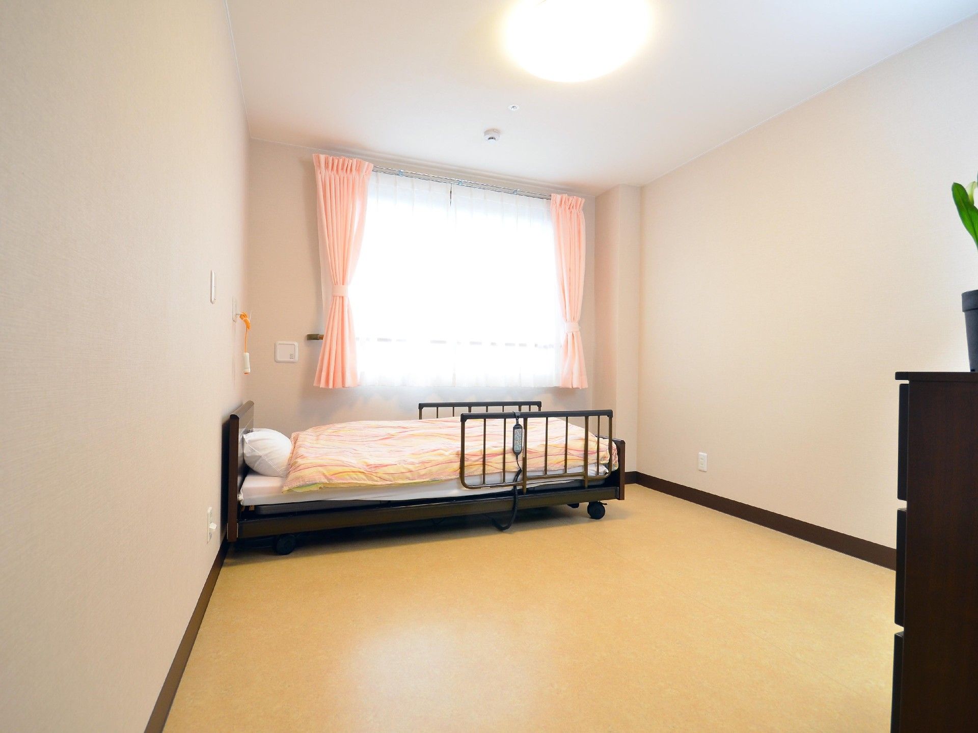 窓から明るい光が差し込む個室である。白い壁にクリーム色の床の部屋で、ベッドわきにはナースコールが設置されている。
