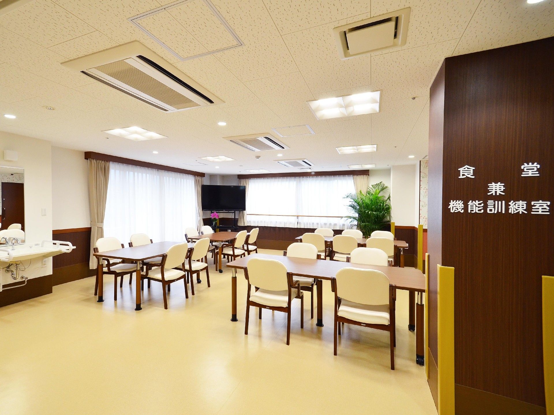 白いフローリングと、白とブラウンの壁の部屋に、落ち着いた色合いの家具が配置されている。また、フットレス仕様の洗面台も設置されている。