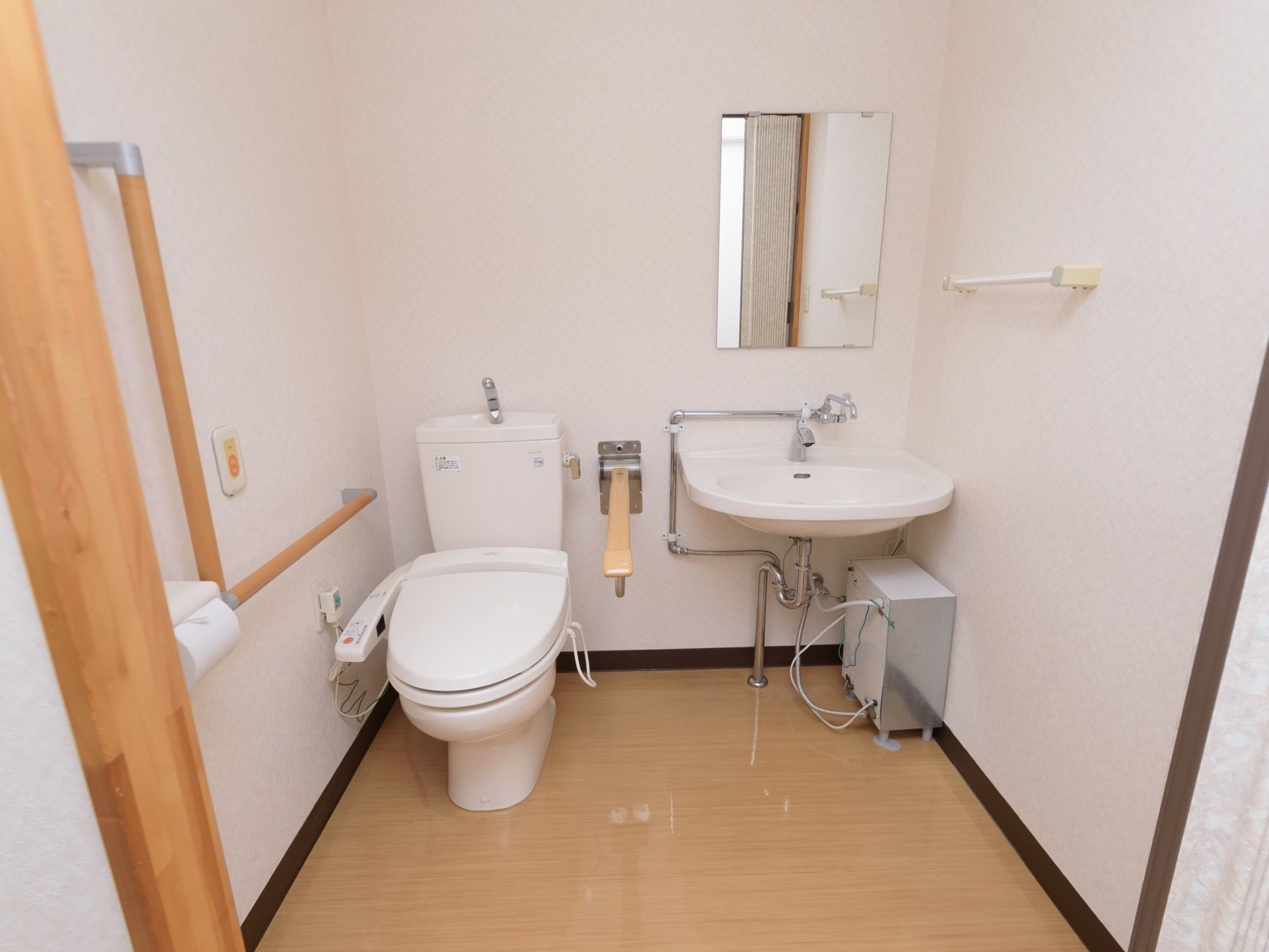 各居室には、洗浄機能付きの洋式トイレと車椅子対応の洗面台がある。入口にスライド式ドアがかかっている。