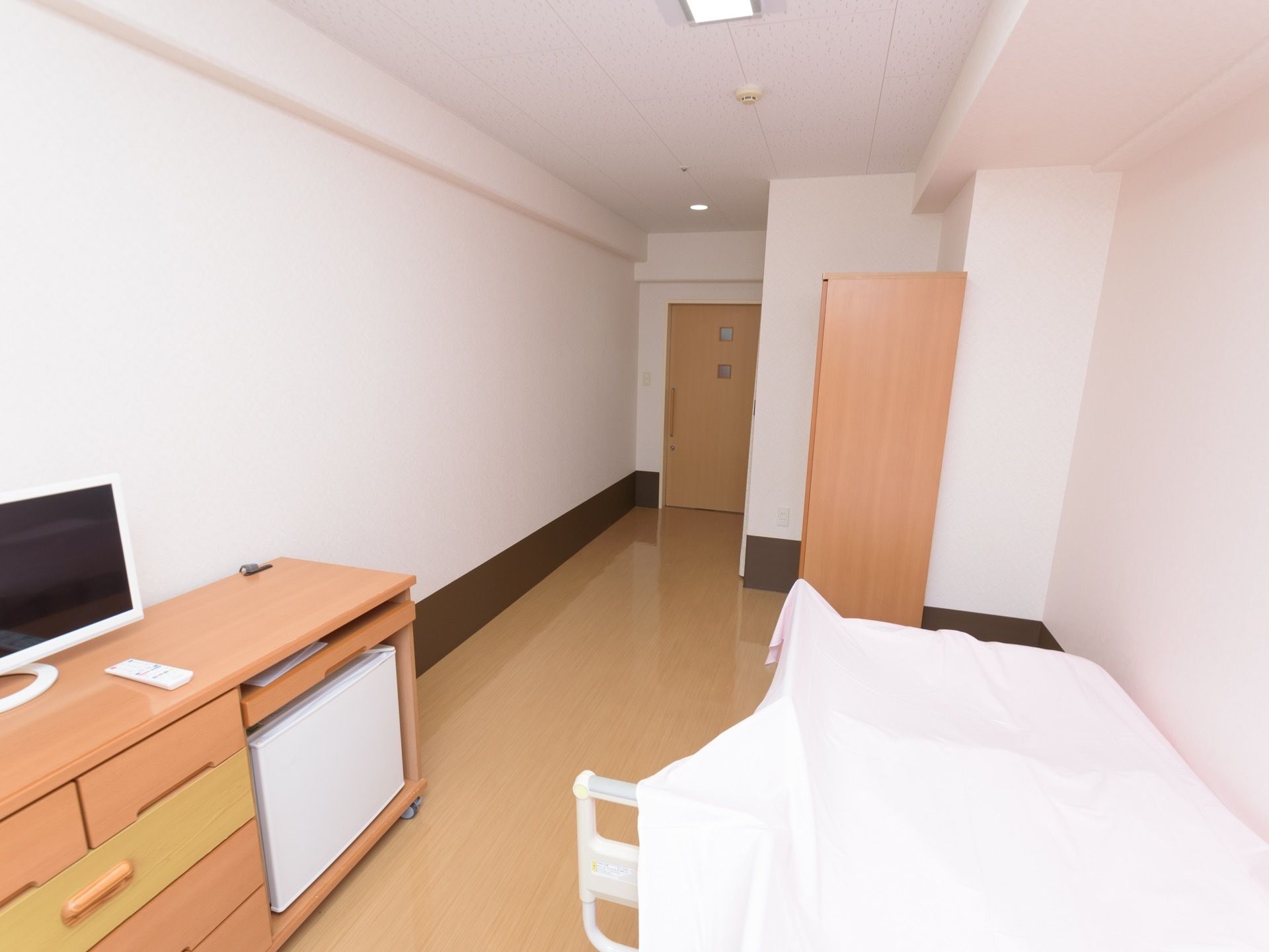 居室には介護用ベッドがある。テレビが置かれている収納家具には、小型の冷蔵庫が収められている。