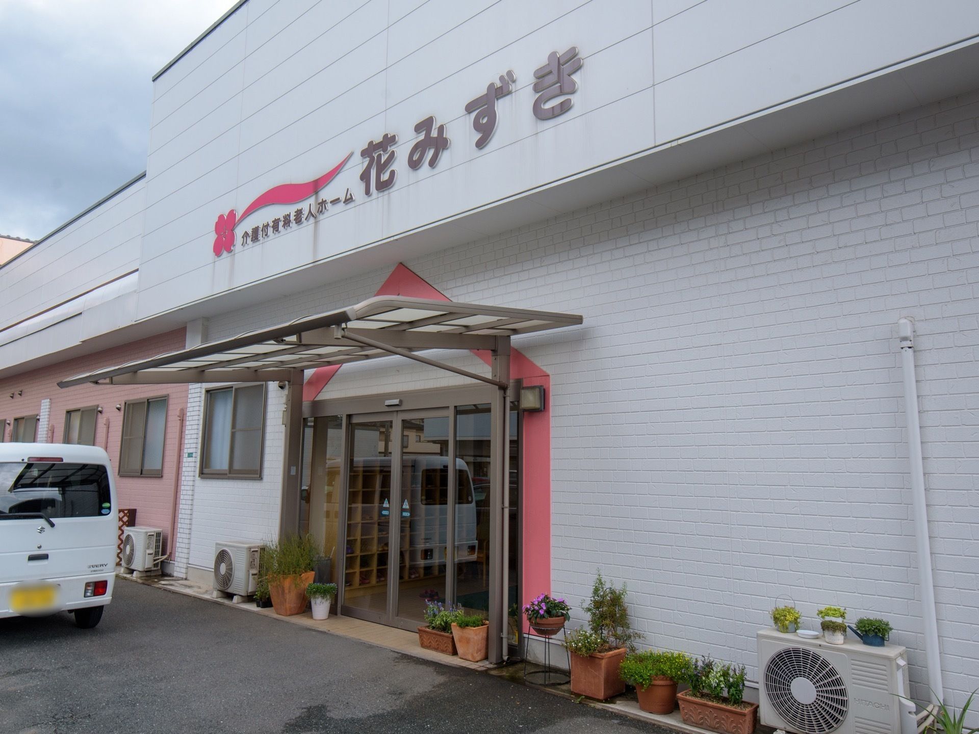 玄関には自動ドアが設置されており、上にはひさしが付いている。ドアの両脇と右側の壁際に、鉢やプランターに植えられた花が置かれている。