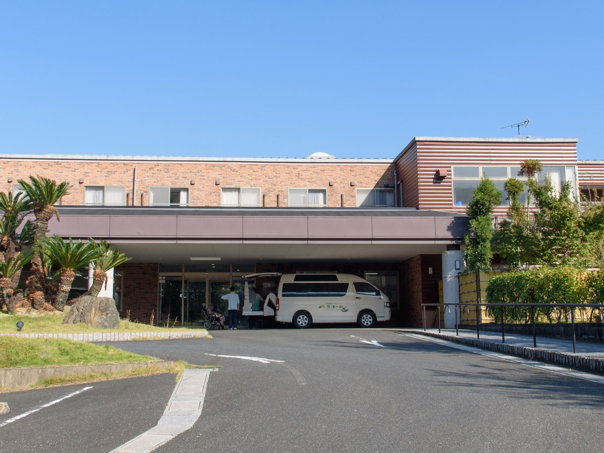 建物の左はタイル状、右は横じまのサイディングになっている。大きなひさしが張り出し、車が乗り入れている。右側に竹垣がある。