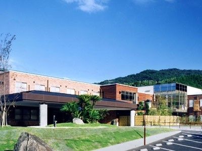 ブラウン系の2階建ての建物は横に長く、手前には駐車場も完備。建物の裏には山もある。
