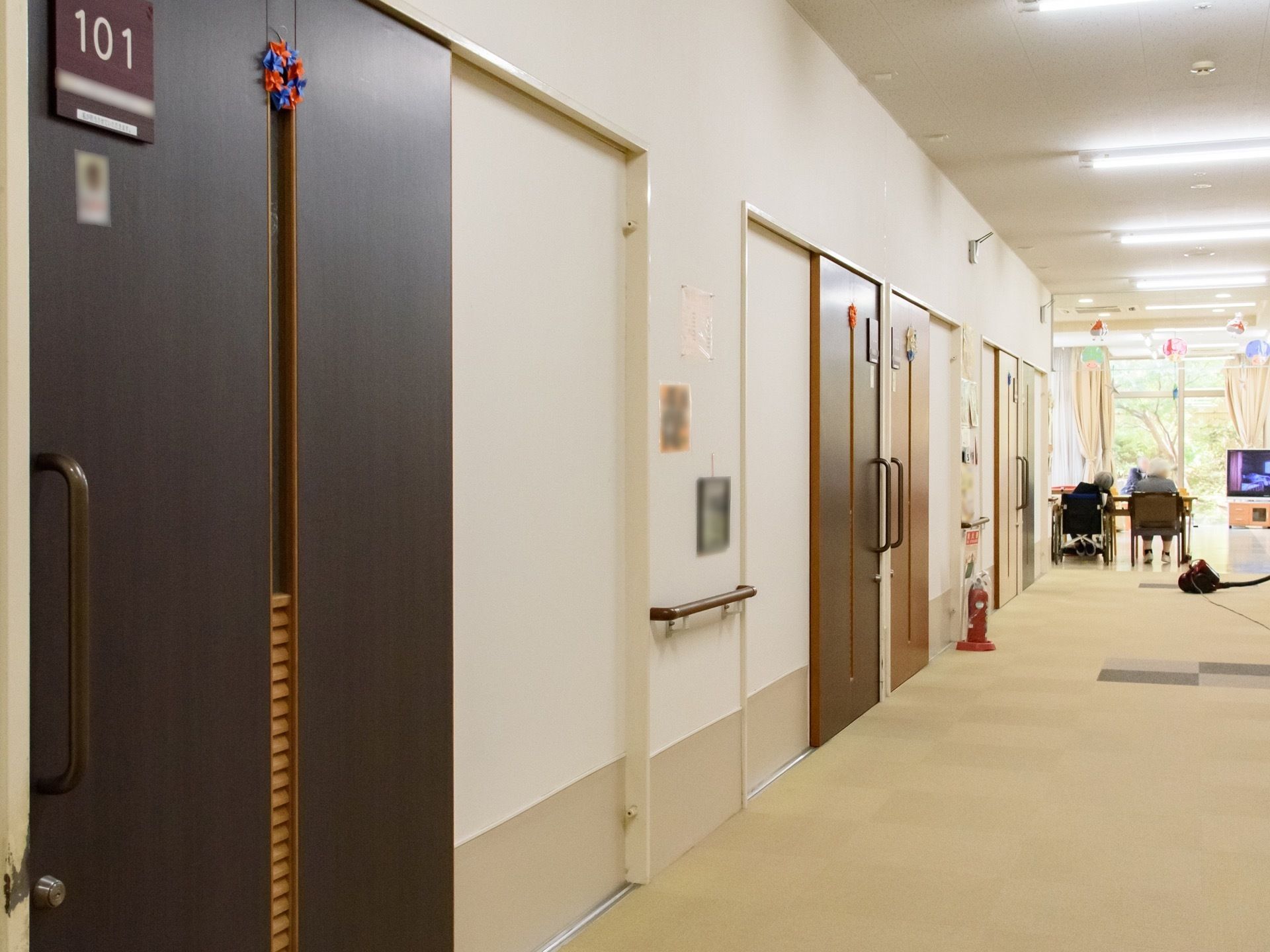 通路はカーペットの床と白い壁。花の飾りのついたダークブラウンの個室のドアが並び、部屋番号が表示されている。