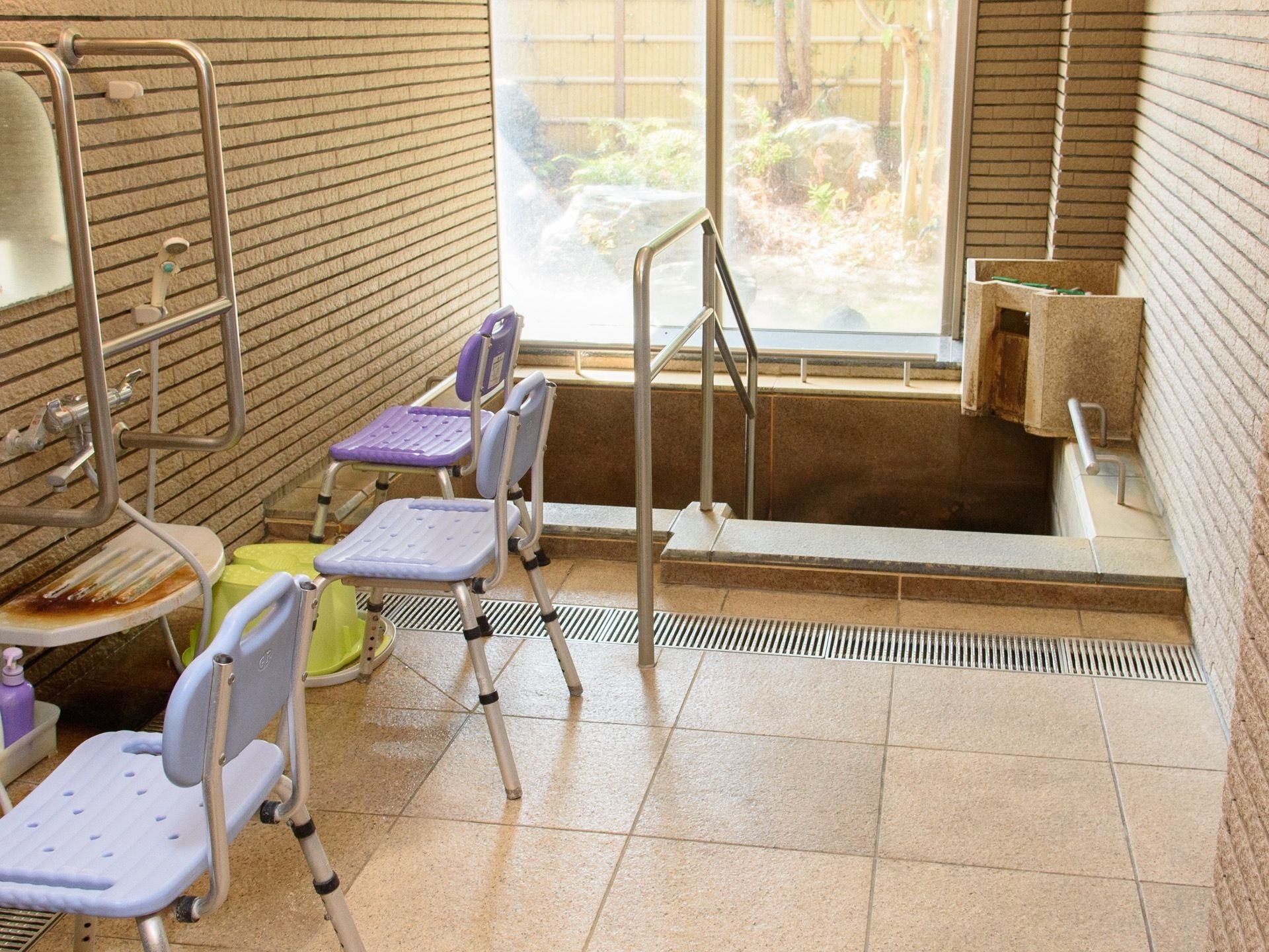 四角い敷石状の床とタイル張りの壁面である。石造りの浴槽があり、手すりが設けられている。大きな窓の外には坪庭が見える。