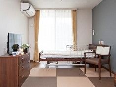 居室にはエアコンが設置され、ベージュのカーテンが付けられた窓があり、ベッドなどが並んでいる。