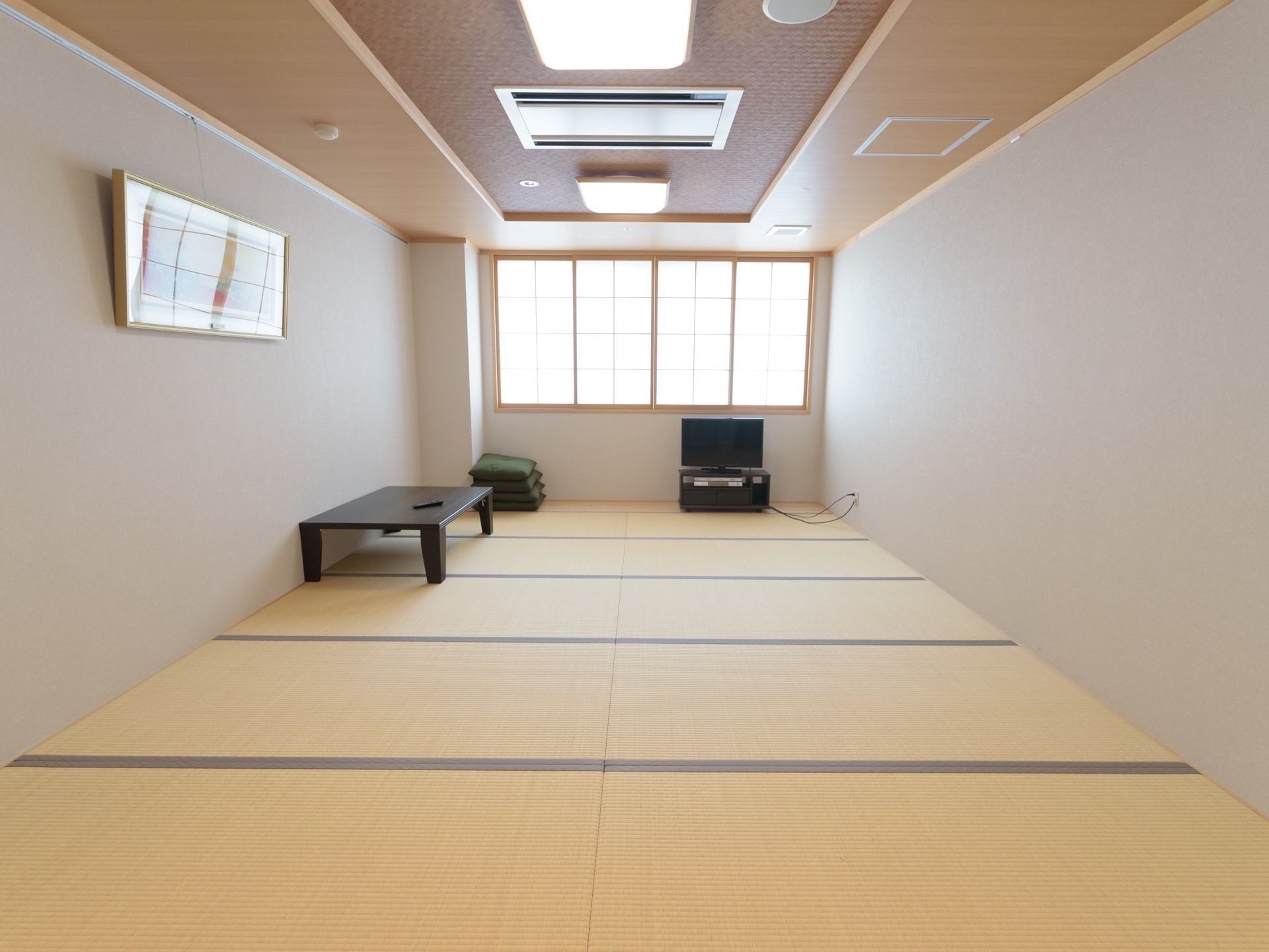 和室には畳が敷き詰められており、テレビやテーブル、座布団が置かれている。左の壁には額に入った絵画が飾られている。