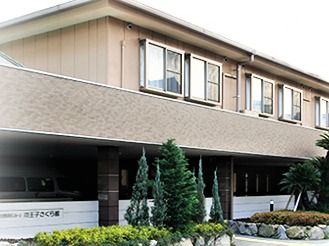 2階建てのベージュの建物。1階部分の一部は駐車場になっている。
