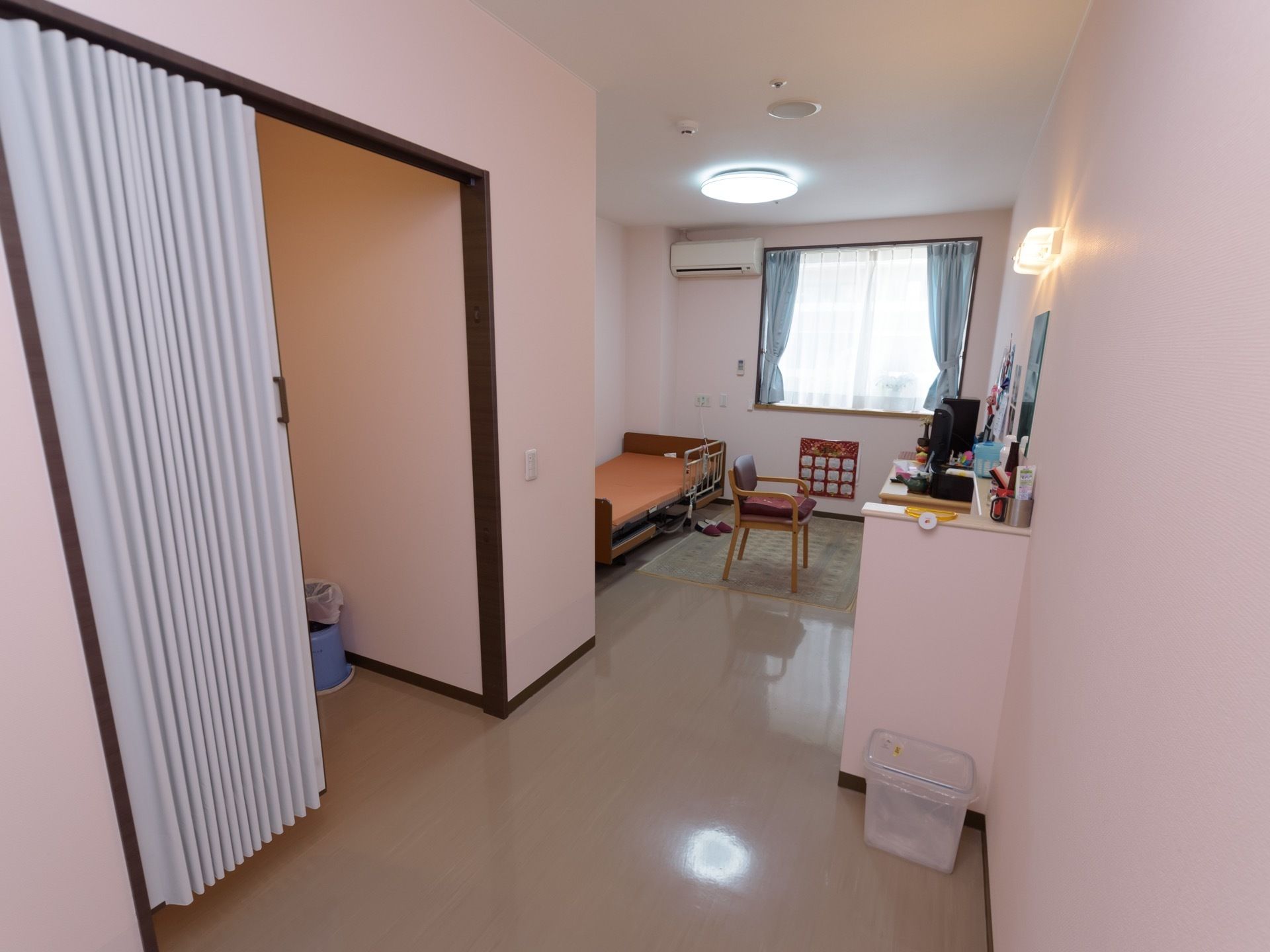 居室内は段差のない造りになっている。左側にはアコーディオンカーテンが取り付けられており、奥のスペースにはベッドや椅子などが置かれている。