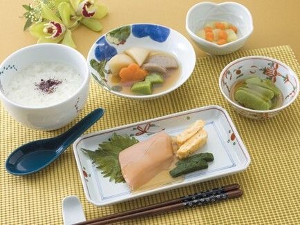 魚料理や煮物がそれぞれの色を活かしたソフト食となって、きれいに器に盛られている。おかゆの前には黒いスプーンが添えられている。