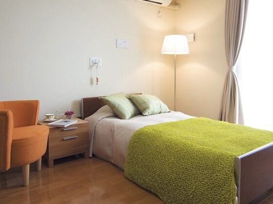 フローリングの部屋には、寝具がセットされたベッドや一人用の椅子、小さなチェストが置かれ、ベッドサイドに緊急通報装置とランプがある。