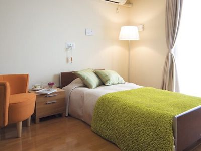 寝具がセットされたベッドや一人用の椅子が設置されたフローリングの部屋には、大きな窓があり、ベッドサイドに緊急通報装置が付いている。