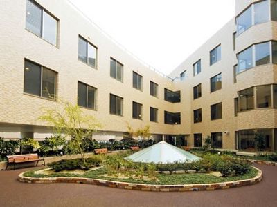 ベージュのどっしりとした大きな建物の前には手入れの行き届いた庭があり、中庭を囲む遊歩道にはベンチも複数置かれている。