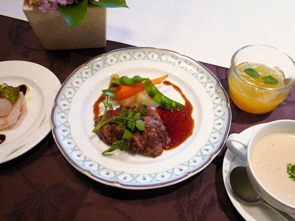 赤ワインソースがかかった肉のソテーをメインとした洋風のコース料理。ポタージュや前菜、フルーツゼリーなどが並んでいる。