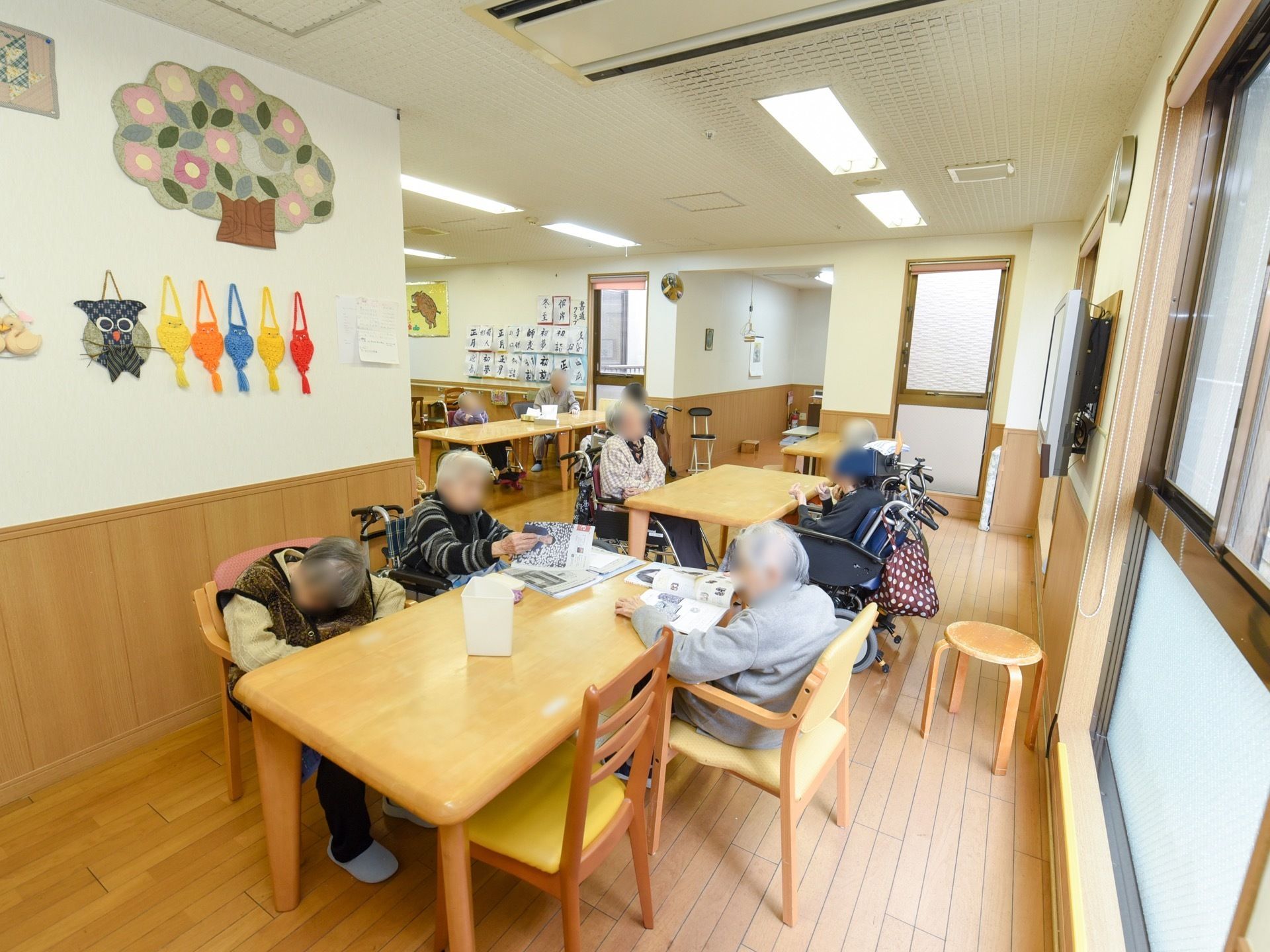 食堂では入居者様が、読書や談笑をしている。壁には書道の作品などが飾られ、大型テレビも掛けられている。