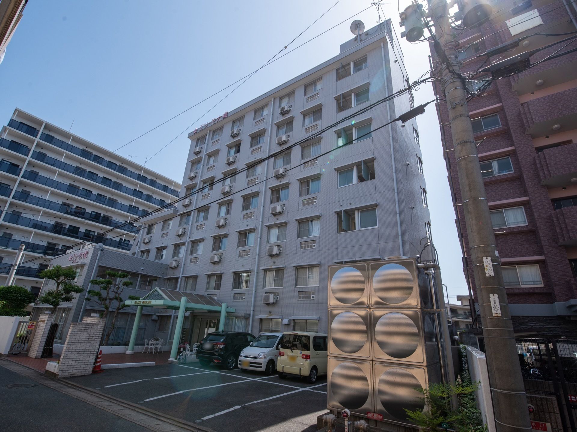 道路沿いに建っている７階建ての施設。両側に同じくらいの高さの建物が並んでいる。敷地内に駐車スペースが８台分ある。