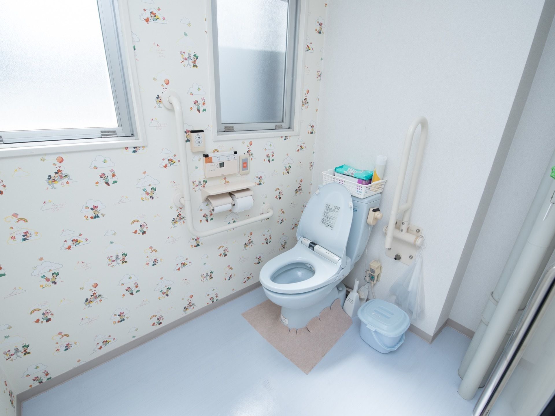 トイレの床面と便器が水色で統一されている。壁には、便座の操作パネルや緊急呼び出しボタンが取り付けられている。
