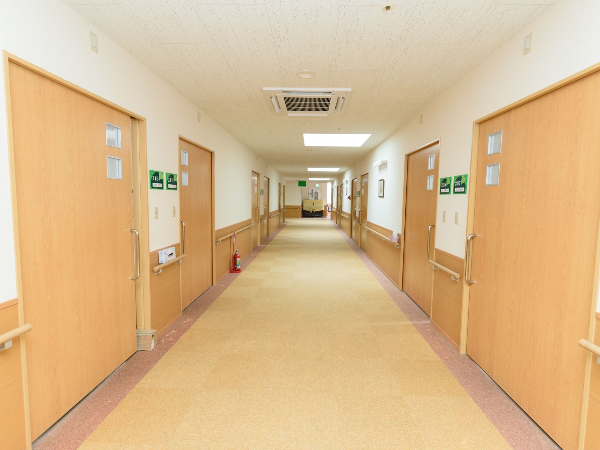 廊下は、所々に配置された大きなライトで明るく照らされている。両側に小窓付きの居室ドアが並んでいる。壁には手すりが設置されている。