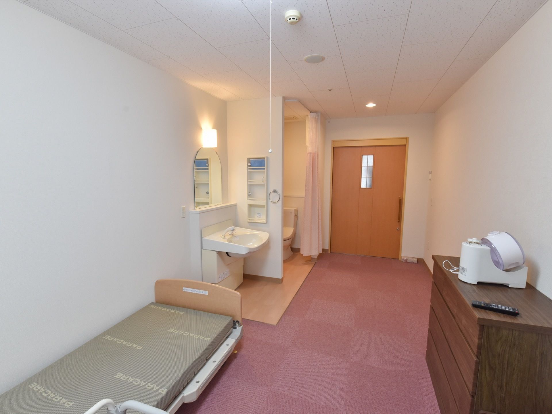 居室内の生活スペースはカーペットが敷かれている。トイレはカーテンで仕切られている。専用の洗面台が設置されている。