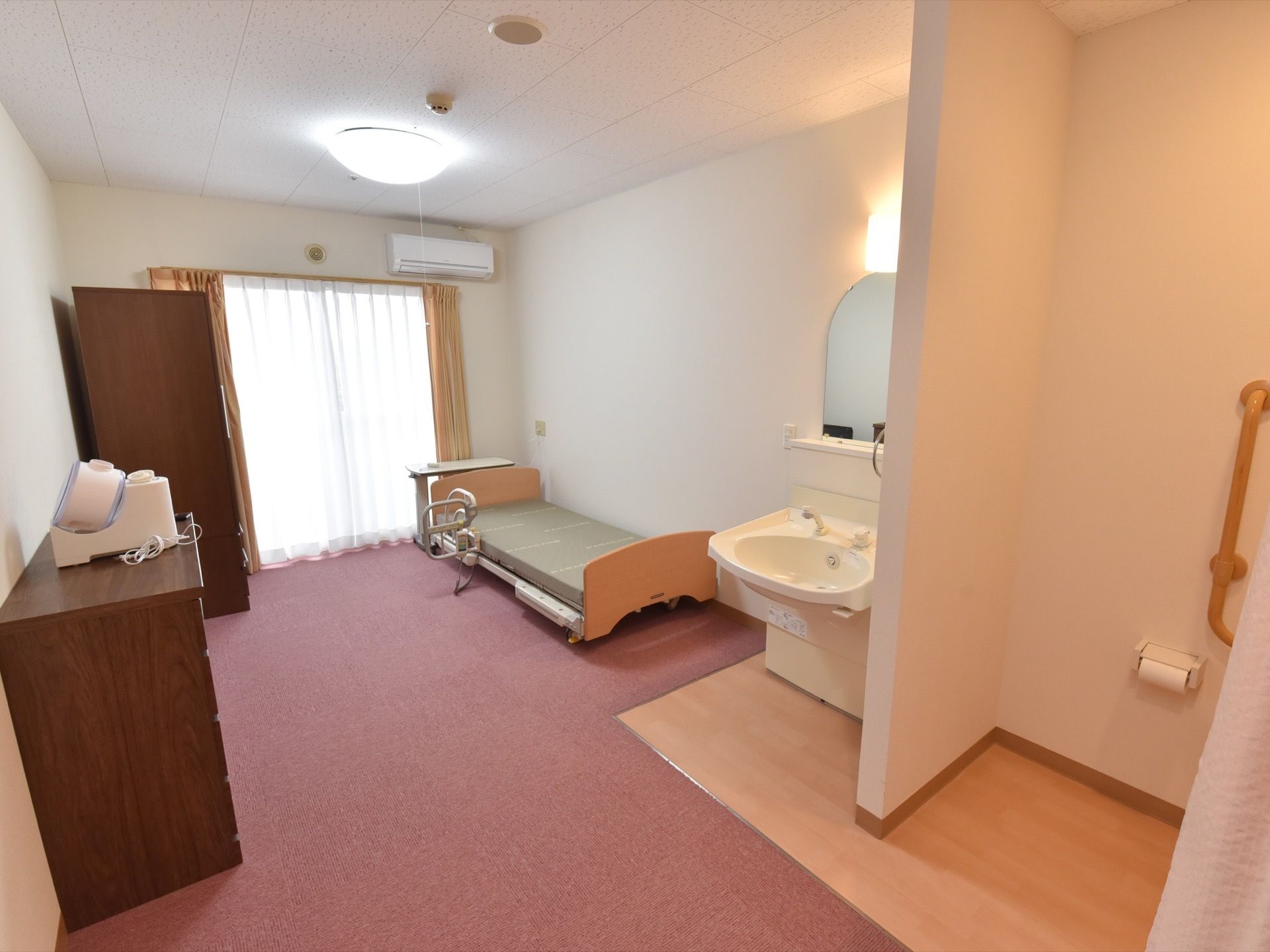 大きな窓がある明るい居室。大型の家具やベッドを置いても広さに余裕がある。洗面台やエアコンが設置されている。