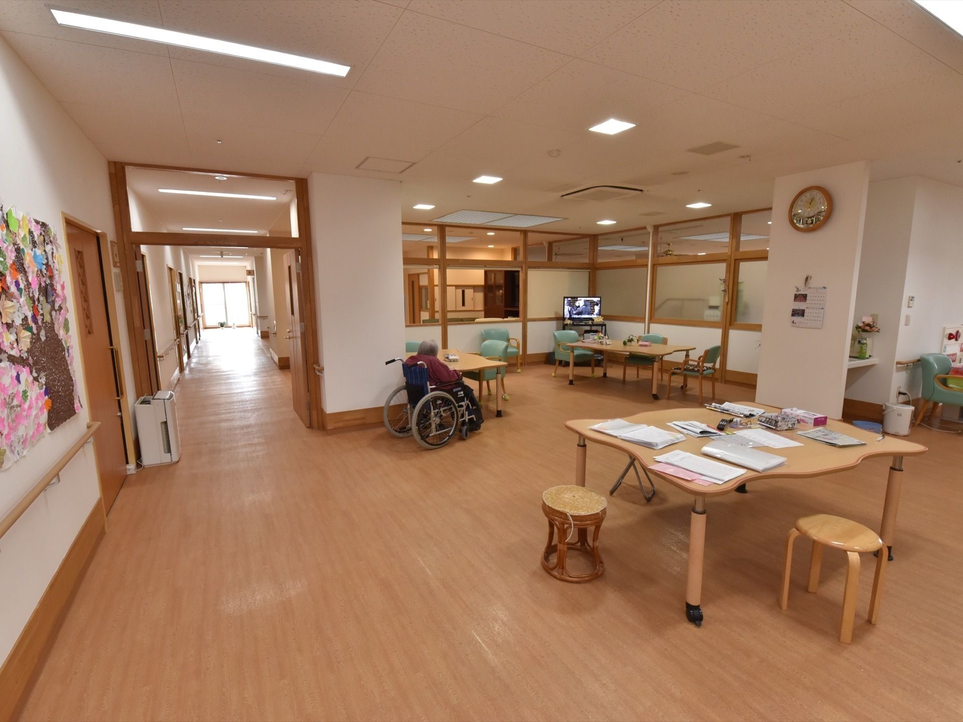 複数のテーブルやイスが並んだダイニングルームで、入居者がテレビを見ている様子