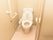 床や壁が白で統一されたトイレがある。壁には手すりが備え付けられており、その近くにはナースコールも付いている。