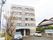 住宅街の一角に、５階建ての施設が建っている。建物の前は、舗装された駐車スペースになっており、車が２台停まっている。