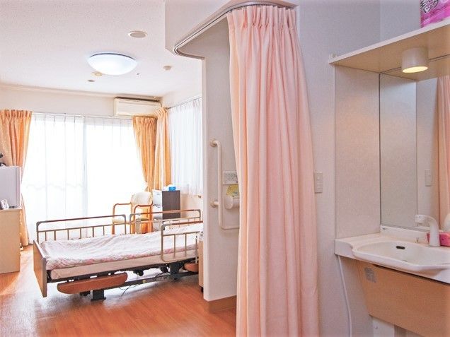 手前に洗面台、奥のほうに介護用ベッドが置いてある施設内の個室の様子