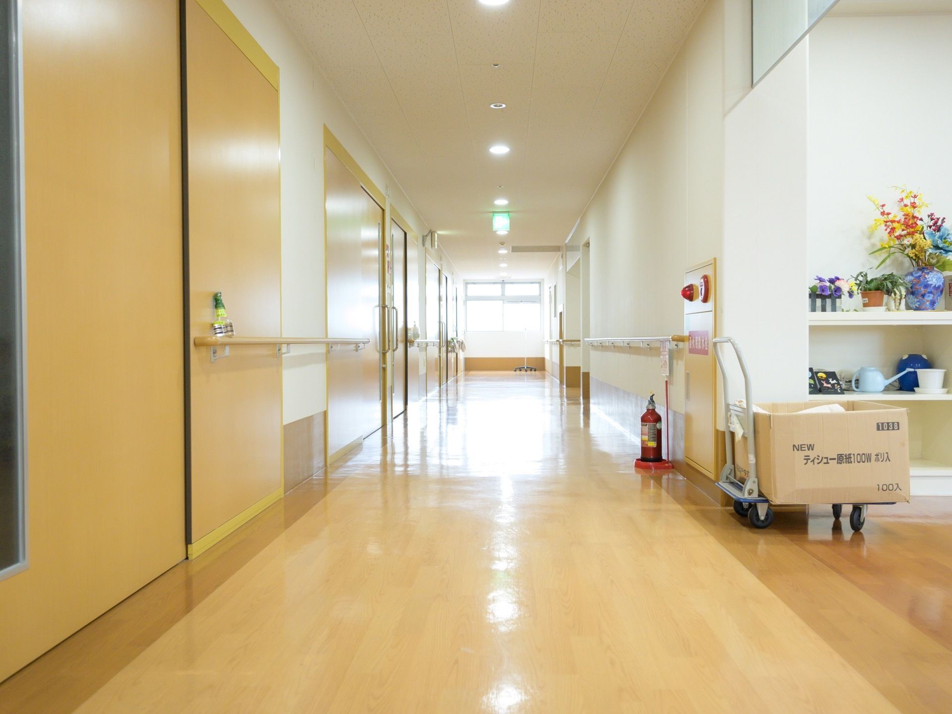 壁は白く、床はベージュ色の通路である。両側の壁に手すりが続いている。火災報知器の側には消火器がある。