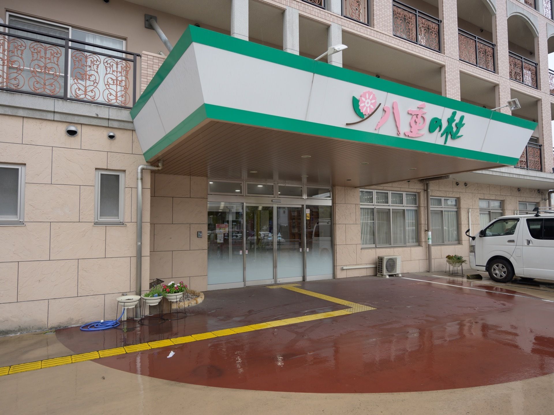 玄関へ続く通路中央に、黄色の点字ブロックがある。玄関は自動扉で大きなひさしがあり、施設名が掲げられている。