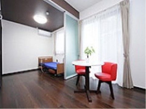 ベッドや白いテーブルと赤い椅子が配置された居室