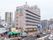 10階建てのビルの壁にカラフルな施設の看板が見える。市街地に建っており、周辺には商店、マンションなどが立ち並んでいる。