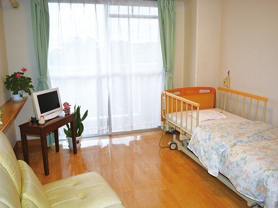 ベッドには布団がセットされ、すぐ近くに窓がある。ソファやテレビなどの家具家電がそろった部屋。