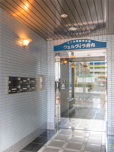 マンションのような雰囲気の建物の入り口付近。ウェルヴィラ府内の看板がある様子