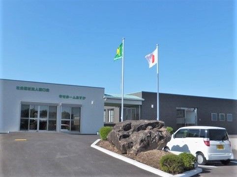 右手には黒、左手には白の建物があり、手前の駐車場には白い車が止まっている。