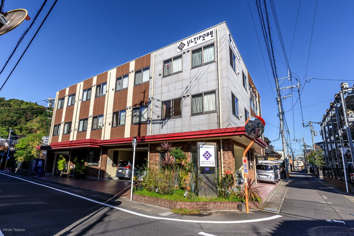 眼鏡をかけた高齢女性が車いすに座り、目の前にいる女性が差し出す手を笑顔で見ている。