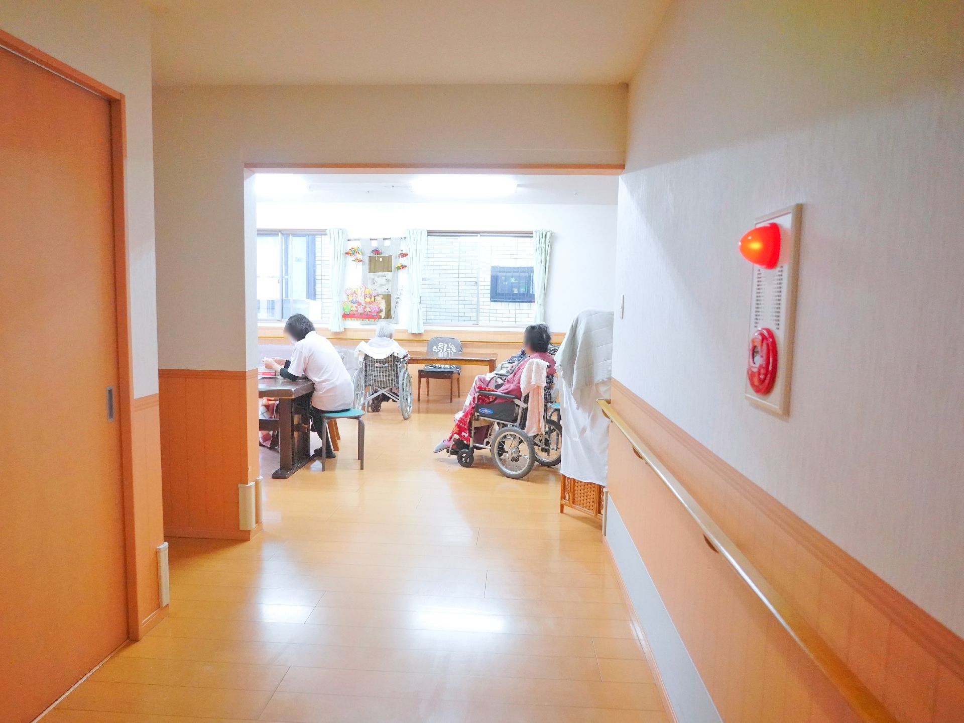 高齢者2名とスタッフが手を握りながら談笑している様子。施設内の会話の一画面