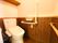 トイレの壁は、下半分が木目調で上半分は白く、温水洗浄便座の上には棚が設置されている。壁には手すりやトイレットペーパーホルダーが備えてある。