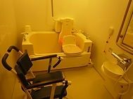 車いすにのる男性とそれを押している女性スタッフ。両側に自然が広がる遊歩道の写真