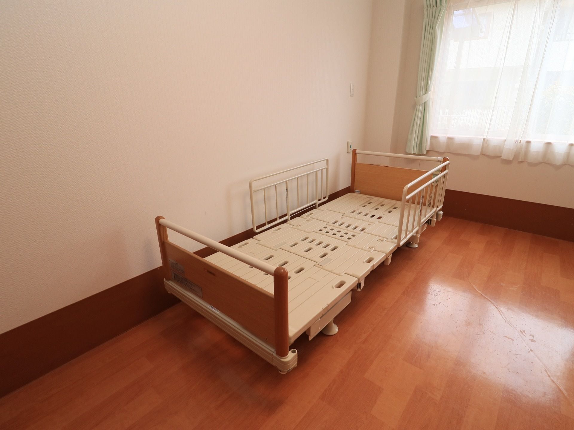 フローリングの部屋に壁際にベッドがある。ベッドの床部分は穴抜きになっており、いくつかに分割されている。両サイドに柵がある。