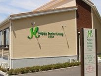 看板の奥にはベージュを基調とした平屋建ての建物が建っていて、周辺には小さな木も植えられている。