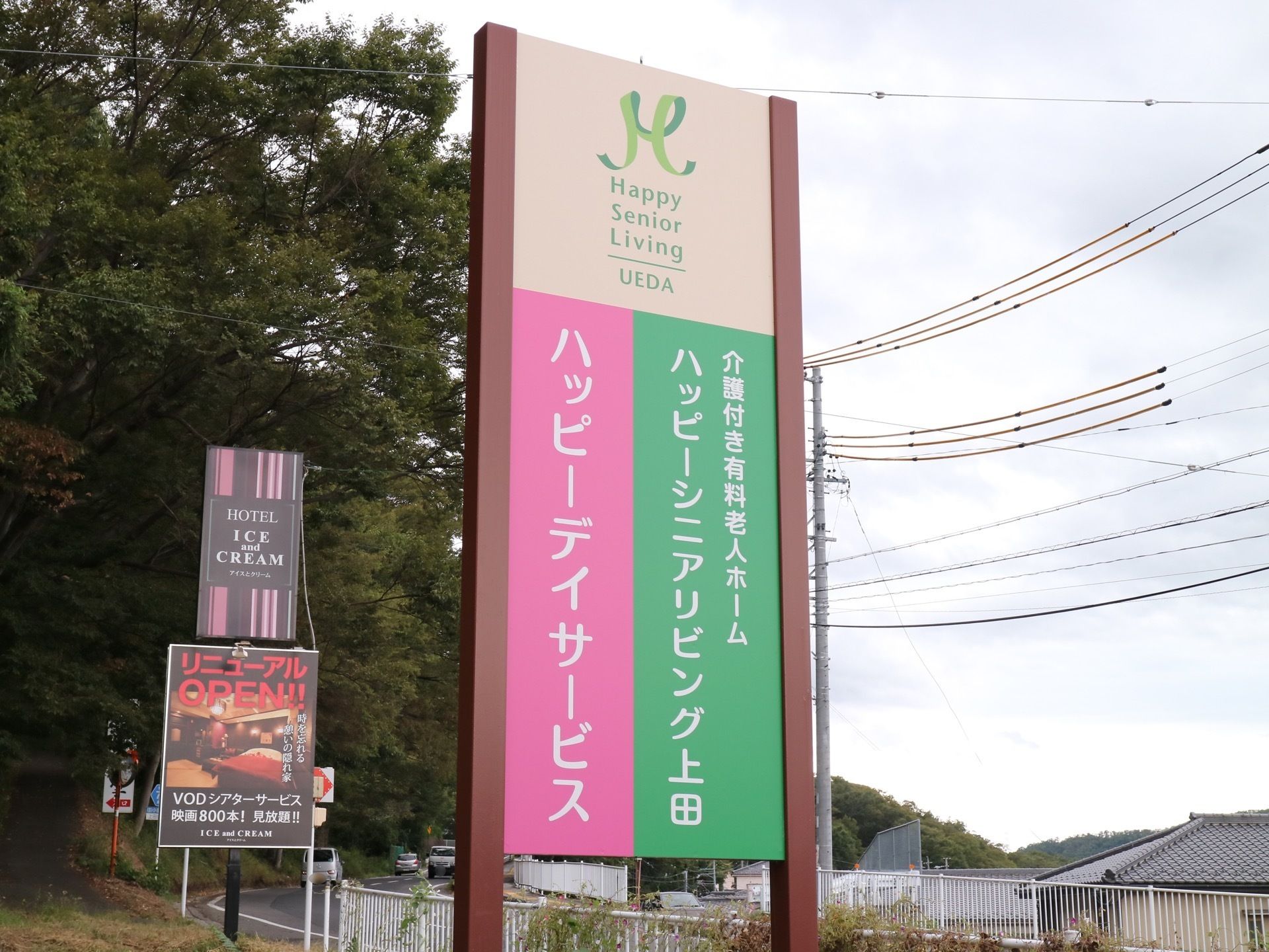 施設の周辺道路に、背の高い大きな看板を立てている。遠くからでも目立つように、ピンクと緑で色分けされている。